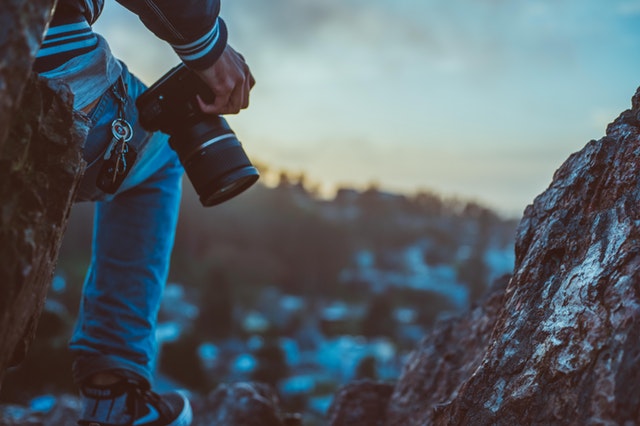 Muž s fotoaparátom v ruke lezie po zasnežených skalách.jpg